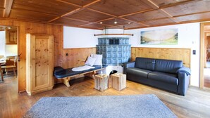Ett mysigt rum med ett träpanelat tak, en svart lädersoffa, en bänk med en vit kudde och en blå öppen spis.