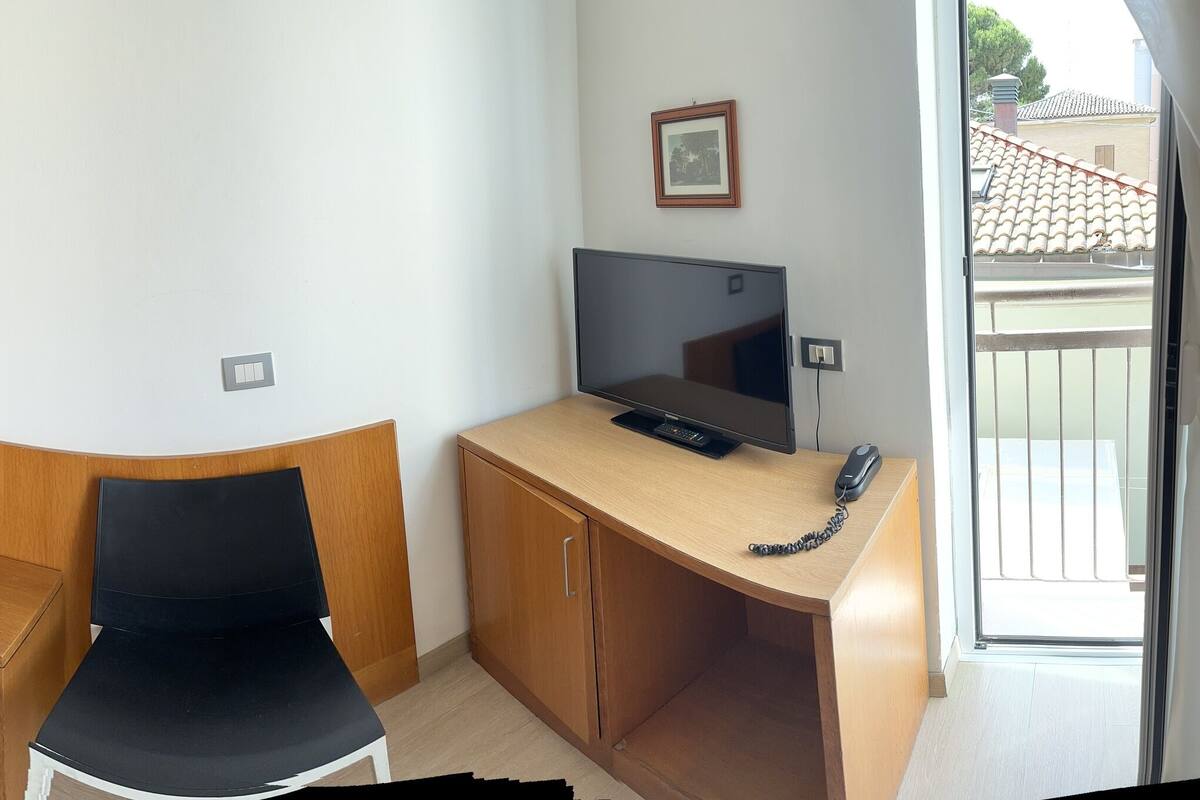 A hotel room with a bed, a desk with a computer, a chair, and a TV.