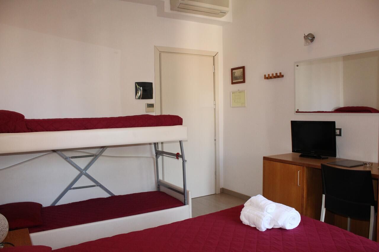 A hotel room with a bunk bed, a desk with a computer, a television, and a mirror.