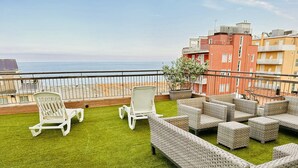 A rooftop terrace with artificial grass, white lounge chairs, wicker sofas, and a view of the sea. - Hotel Morolli Rimini (Rimini)