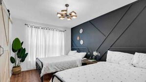 A bedroom with two beds, a ceiling light fixture, a large plant, and a window with curtains.