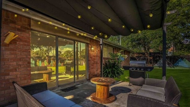 An outdoor patio area with wicker furniture, a round wooden table, and a barbecue grill.