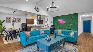 A modern living room with a blue sofa set, a coffee table, and a green wall with a neon sign.