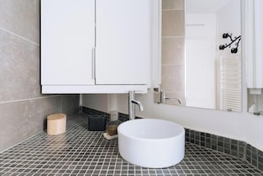 Une salle de bain avec un lavabo blanc, un miroir et un meuble.