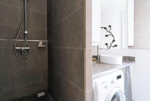 A bathroom with a shower, a sink, and a washing machine.