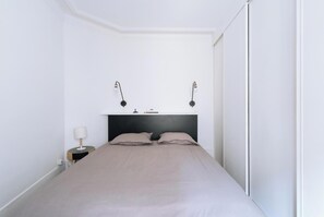 Un dormitorio con cama, dos lámparas de noche, una mesita de noche y un estante en la pared.