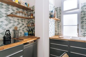 A kitchen with wooden shelves, a kettle, and a sink.