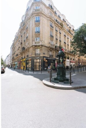 Un edificio de varios pisos con entrada en esquina, una tienda a la calle y un hidrante verde.