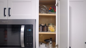 Una cocina con un microondas Whirlpool, una repisa con frascos y utensilios de cocina, y un hervidor.