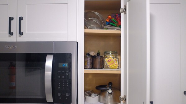 Una cocina con un microondas Whirlpool, una repisa con frascos y utensilios de cocina, y un hervidor.