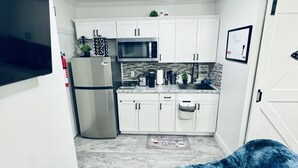 Cocina pequeña con armarios blancos, microondas y refrigerador. Hay un tapete pequeño y un felpudo azul en el suelo.
