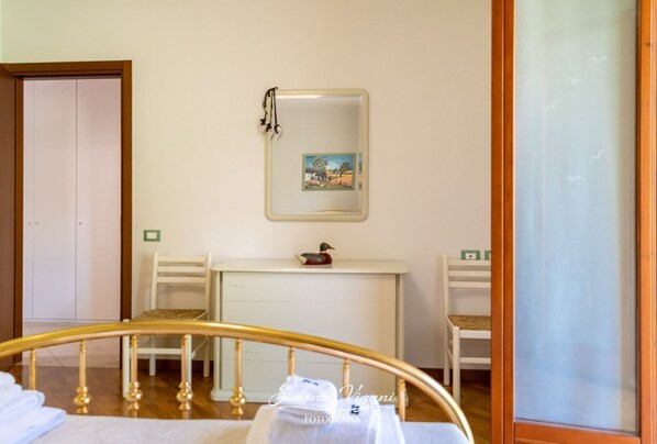 A bedroom with a bed, a bedside table, a chair, a desk, and a mirror.