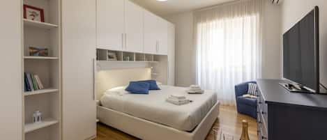 A modern bedroom with a bed, a TV, a minibar, and a bookshelf.