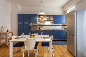 A modern kitchen with blue cabinets, a stainless steel refrigerator, and a dining table set for four. - Strigelli, 13 - Accogliente bilocale con balcone (Milano)