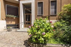 Una entrada empedrada con un parterre de flores, una puerta y una ventana con contraventanas.