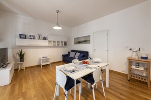 A modern living room with a dining table set for four, a sofa, a TV, and a bookshelf. - Strigelli, 13 - Accogliente bilocale con balcone (Milano)