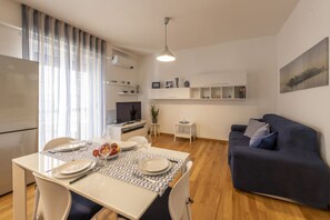 A modern living room with a dining area, a sofa, a TV, and a kitchen area.