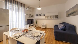 Uma sala de estar moderna com área de jantar, sofá, televisão e cozinha.