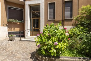 A stone-paved entrance with a flower bed, a door, and a window with shutters. - Strigelli, 13 - Accogliente bilocale con balcone (Milano)