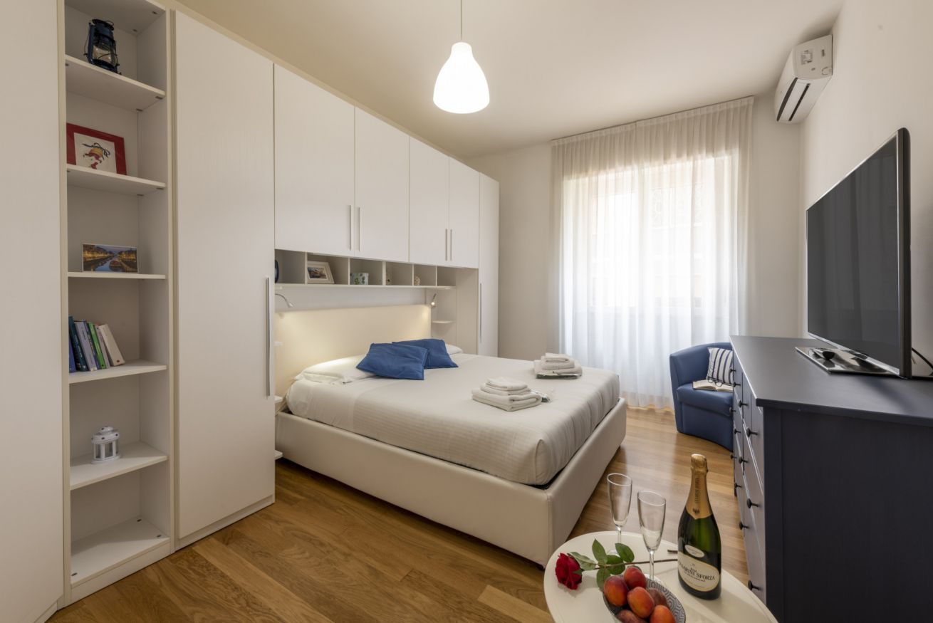 A modern bedroom with a bed, a TV, a minibar, and a bookshelf.