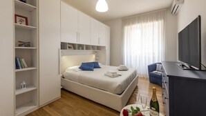 Quarto moderno com cama, televisão, frigobar e estante de livros.