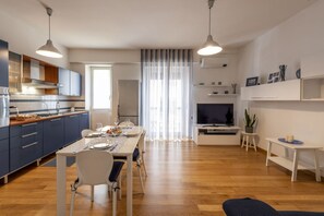 A modern kitchen with a dining area, a TV, and a small table with decorative items.