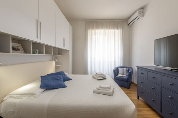 A hotel room with a bed, a TV, a chair, and a wardrobe.