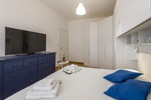 A bedroom with a bed, a TV on a dresser, a small table with a bottle and glasses, and a closet.