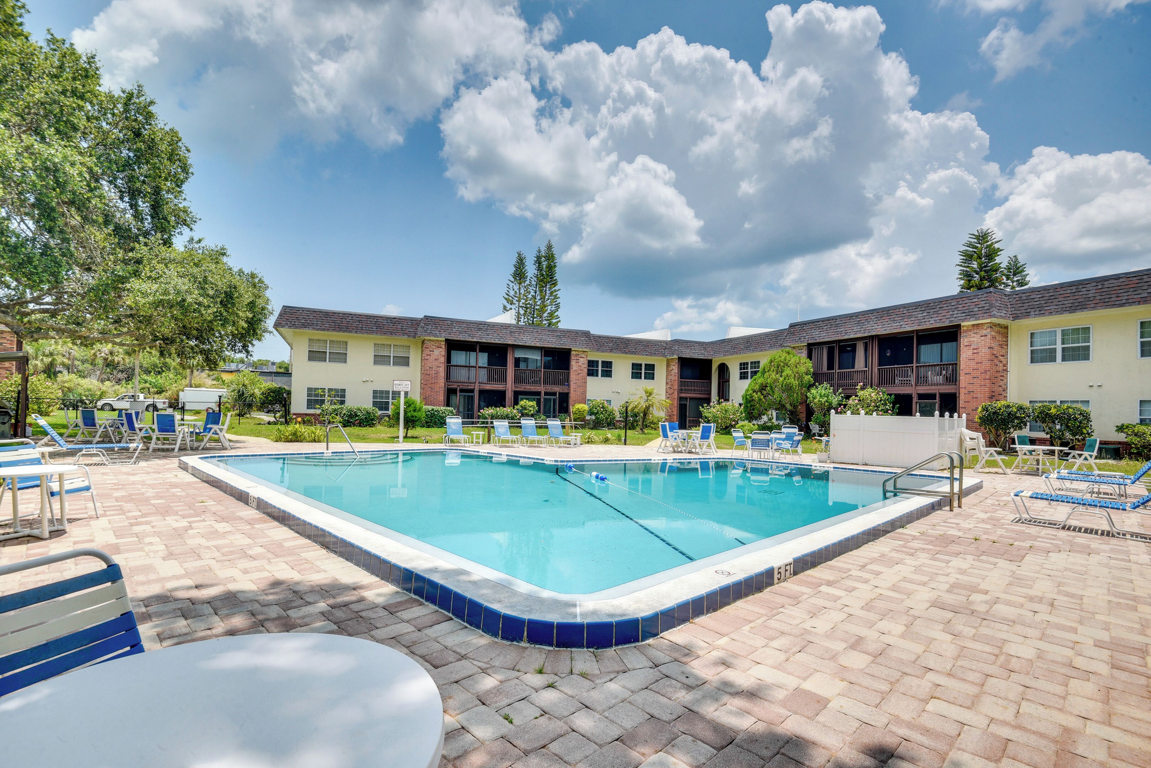 A rectangular swimming pool with a tiled edge, surrounded by lounge chairs and a brick patio.