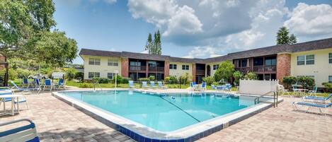 A rectangular swimming pool with a tiled edge, surrounded by lounge chairs and a brick patio.