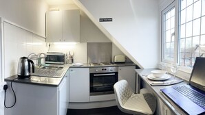 A compact kitchen with a built-in oven, a kettle, and a laptop on the counter. - Big Loft in the Heart of Cheam Village (35 min from London City) (Sutton)