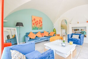 Een ruime woonkamer met een blauwe zithoek, een witte salontafel en een schilderij van rode tulpen aan de muur.
