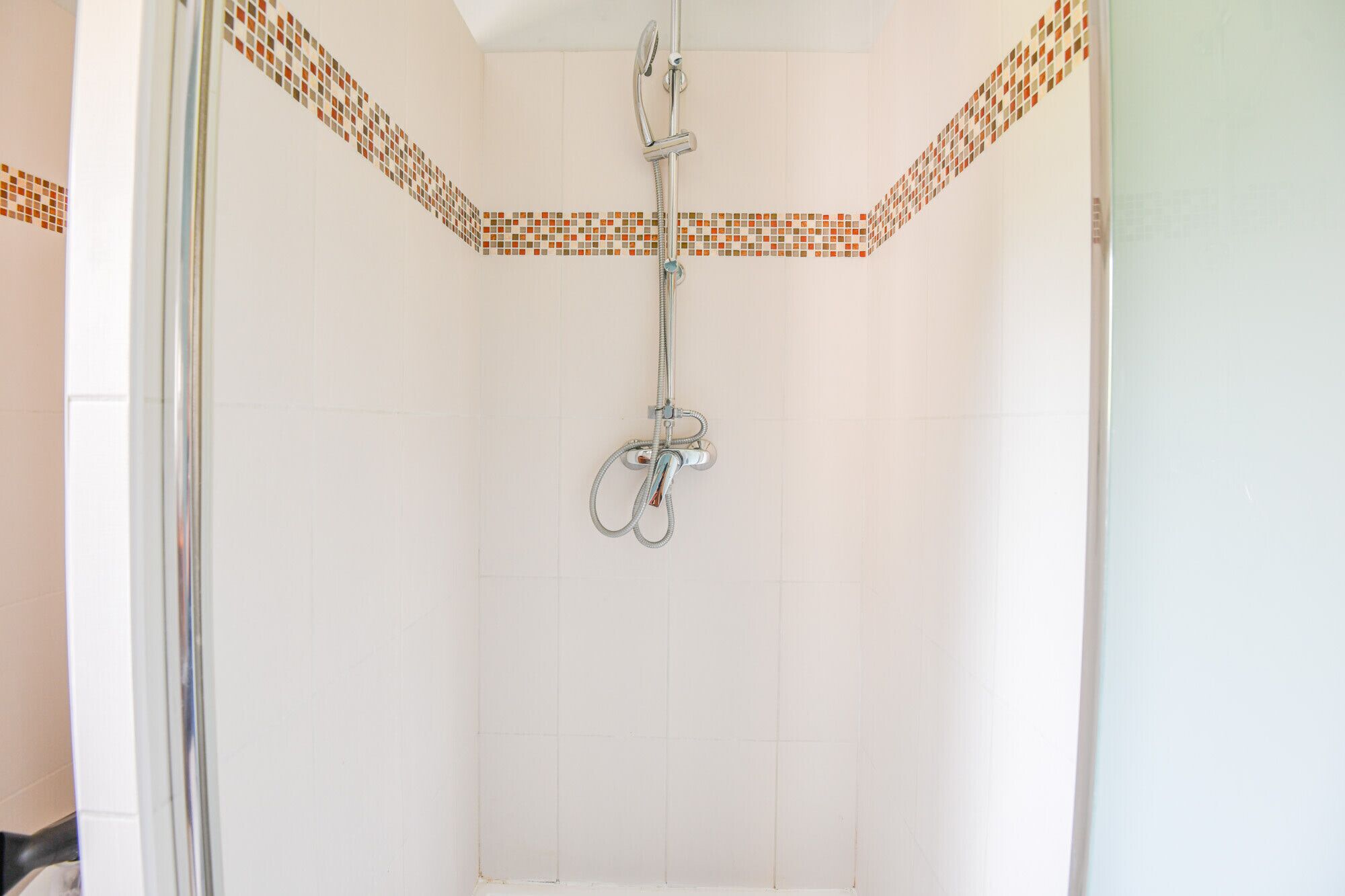 Une douche équipée d’un pommeau de douche chromé et d’un flexible de douche.