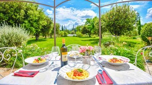 An outdoor dining setup with a table, chairs, and a view of a lush garden and golf course. - Mas des Chênes Verts – 5 ch avec piscine et clim (Eygalières)