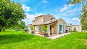 A stone house with a tiled roof, a covered patio, and a well-maintained lawn. - Mas des Chênes Verts – 5 ch avec piscine et clim (Eygalières)