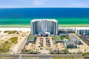 A high-rise hotel with a parking lot and a beach view.