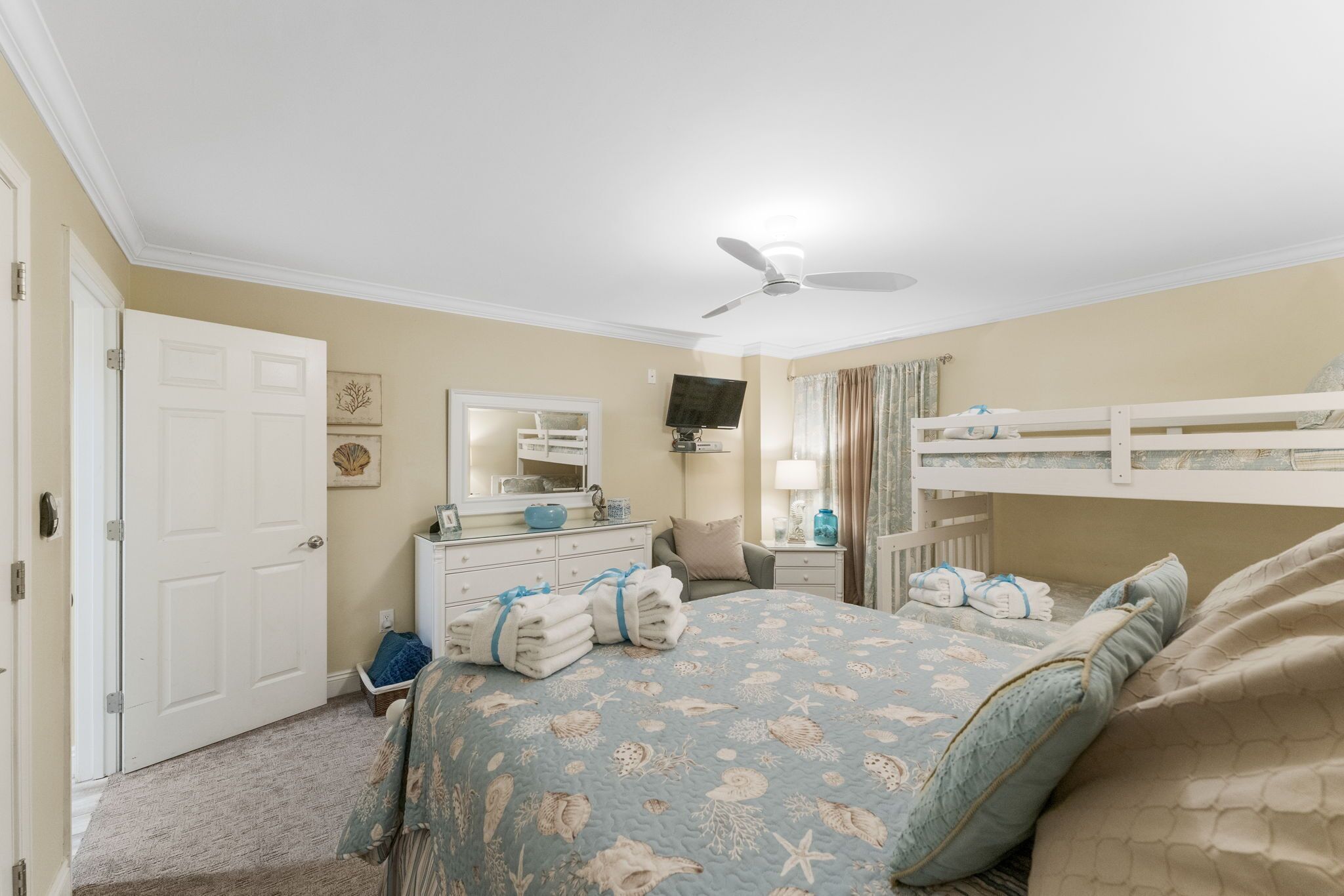A bedroom with a bunk bed, a dresser, a mirror, a ceiling fan, and a door.