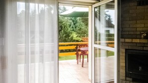 A sliding glass door leading to an outdoor patio with a wooden table and chairs, a green umbrella, and a brick fireplace.