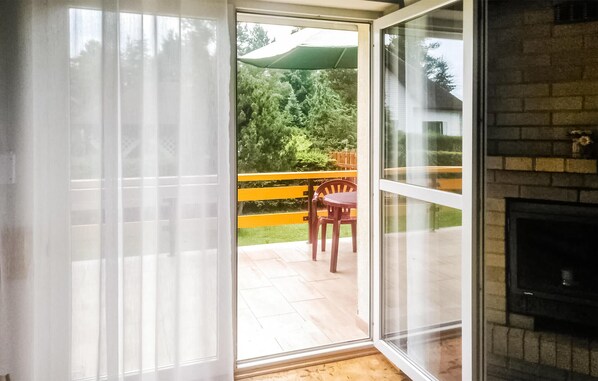 A sliding glass door leading to an outdoor patio with a wooden table and chairs, a green umbrella, and a brick fireplace.