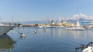 Ein Hafen mit verschiedenen Schiffen, ein Riesenrad und eine gebirgige Kulisse.