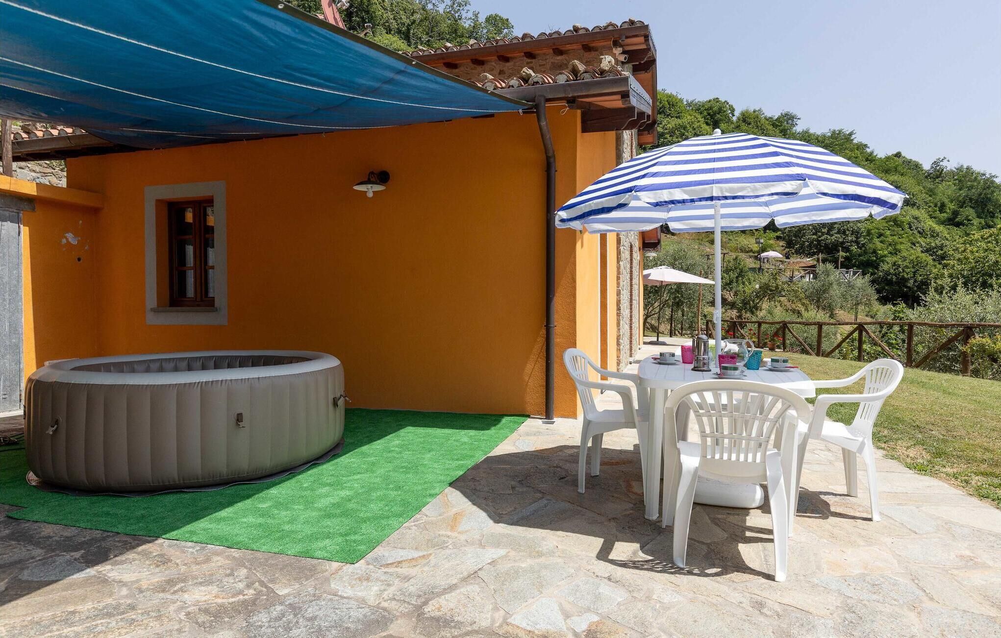An outdoor patio with a hot tub, a table with chairs, and a striped umbrella.