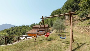 Eine rustikale Holzschaukel auf einer grünen Wiese, im Hintergrund ein traditionelles Haus.