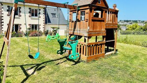 Une cabane en bois avec une balançoire, installée dans une cour verdoyante.