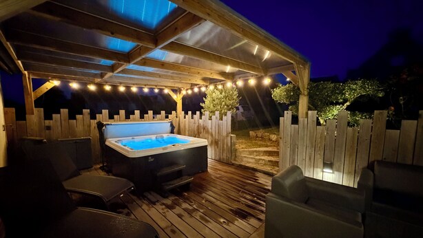 Une terrasse en bois avec un jacuzzi, des sièges d’extérieur et des guirlandes lumineuses.