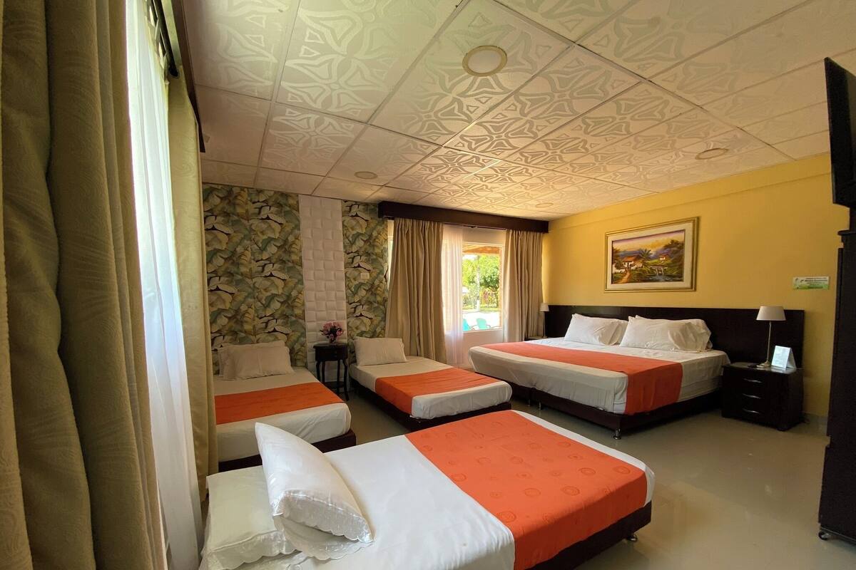 A hotel room with three beds, a painting on the wall, and a window with curtains.