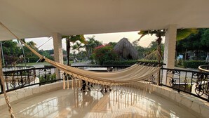 A hammock on a tiled balcony with a view of a garden and a thatched-roof structure. - Hotel Rosalinda Campestre del Llano (Villavicencio)