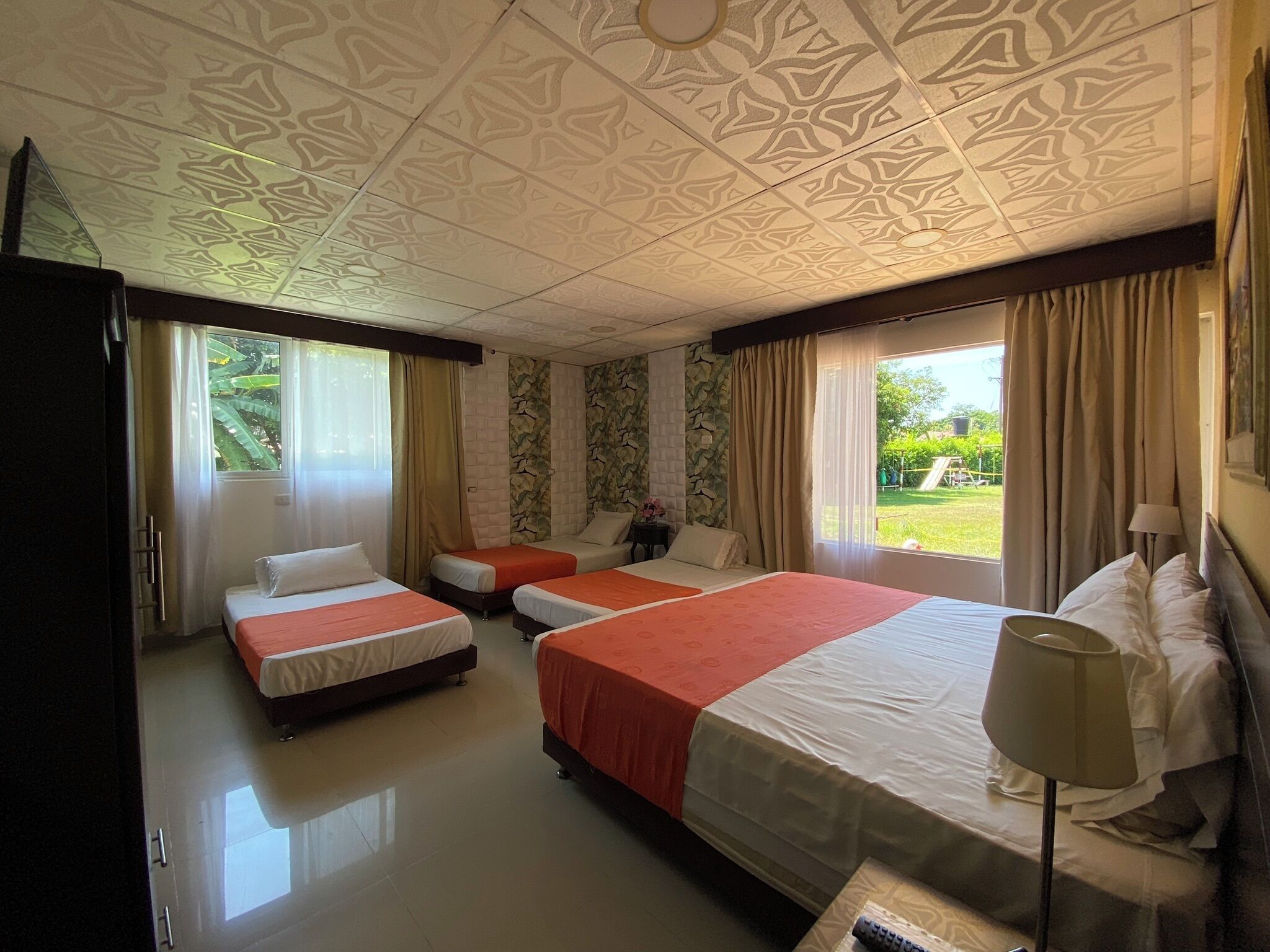 Habitación de hotel con tres camas, un ventanal grande con cortinas, una pared de piedra y un techo con diseño geométrico.