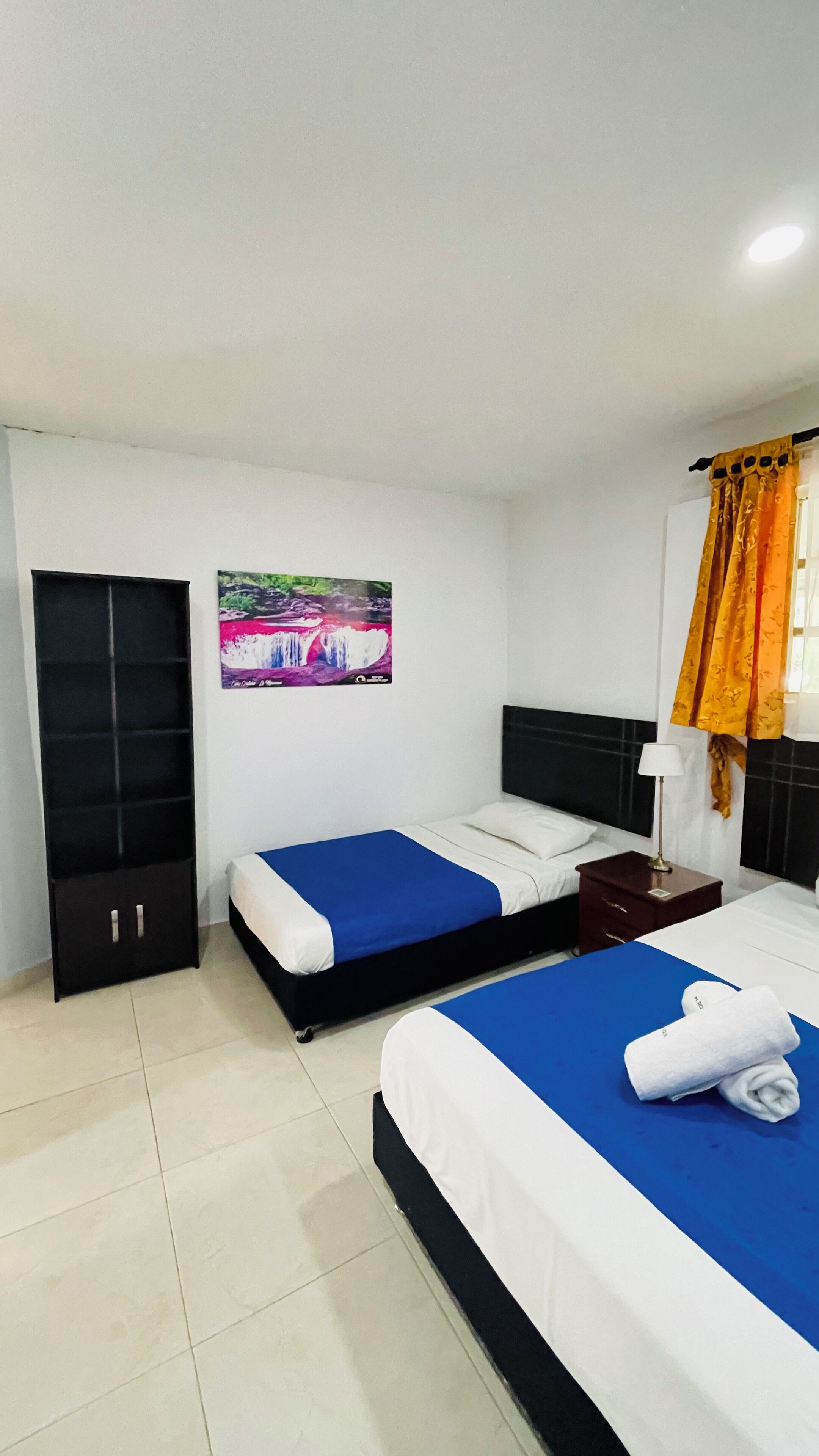 Habitación de hotel con dos camas, un armario, una mesita de noche, una lámpara y un cuadro de una cascada.