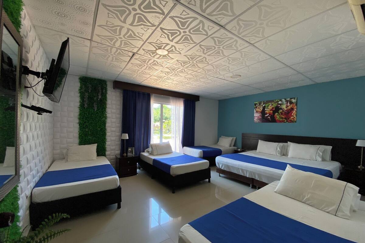 A hotel room with four beds, a TV mounted on the wall, a decorative ceiling, and a window with curtains.