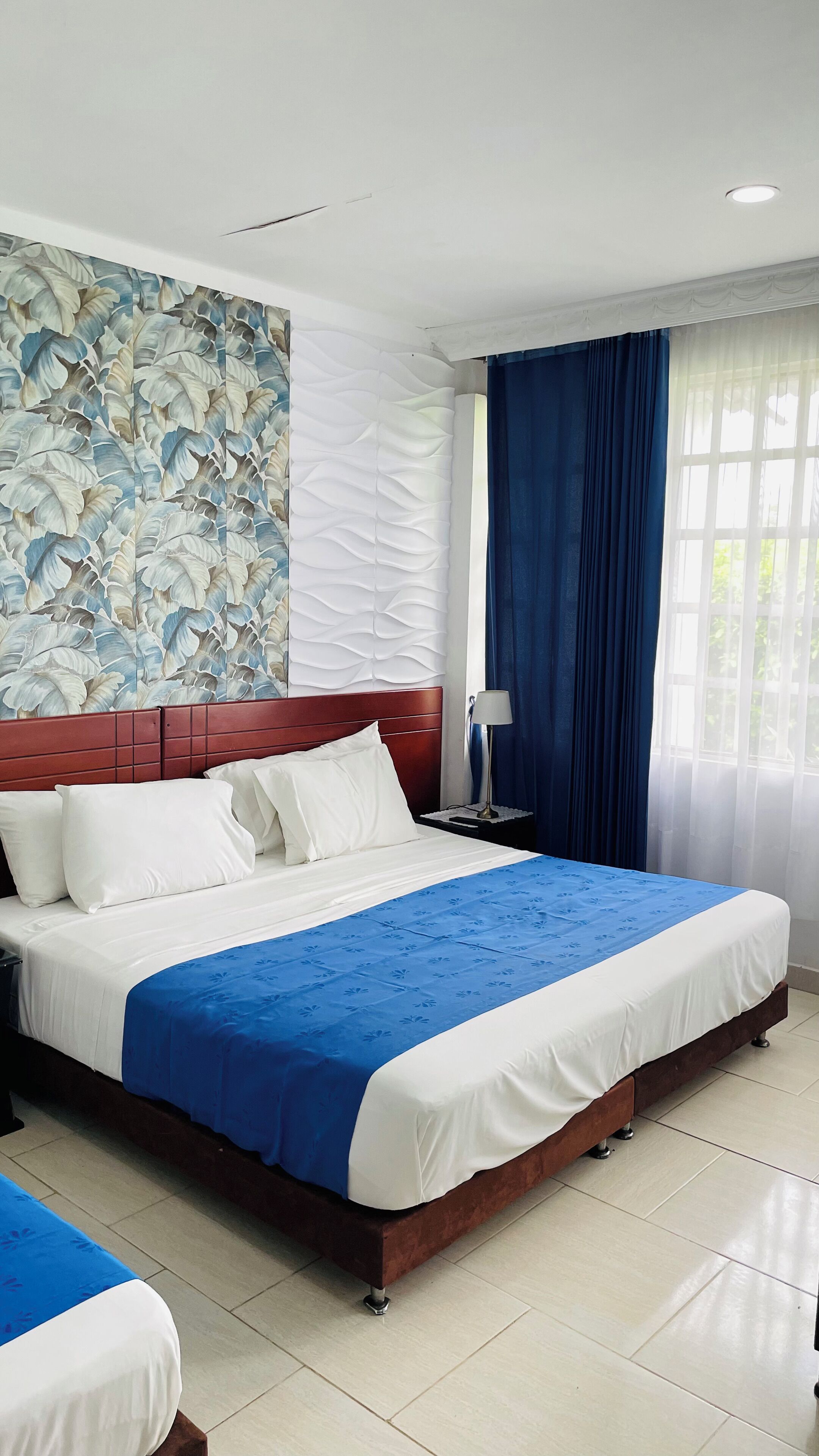 Habitación de hotel con una cama grande, una mesita de noche, una lámpara y una ventana con cortinas.